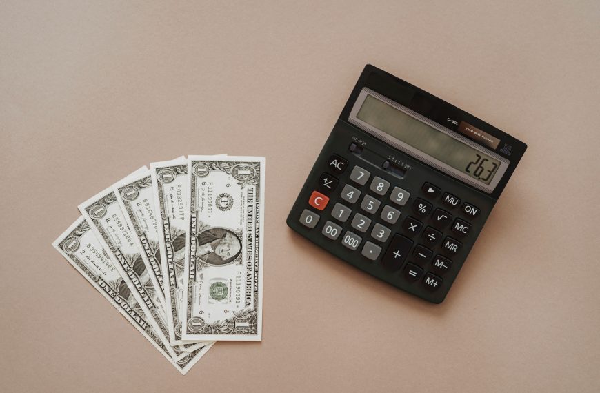 A calculator displaying '26.3' beside four one-dollar bills on a beige background.