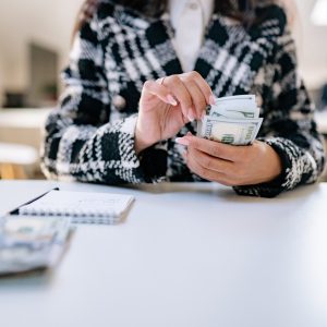 A close-up of a woman counting US dollars in an office environment, symbolizing financial management.